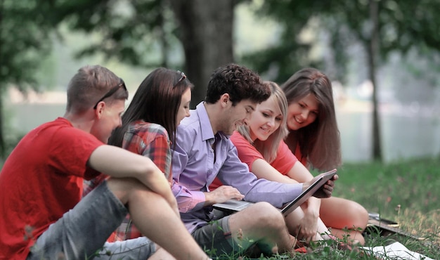 Gruppe Studenten mit einem Laptop, der auf dem Gras im Park sitzt