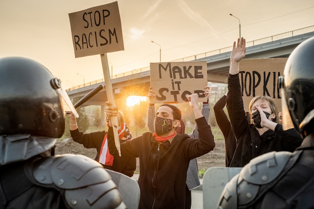 Foto gruppe unzufriedener menschen in gesichtsmasken, die banner halten und für ihre rechte kämpfen, polizei kontrolliert diese aktion