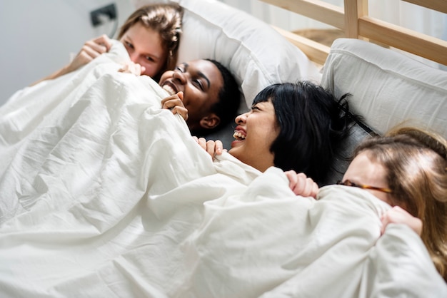 Gruppe verschiedener Frauen, die zusammen unter der Decke auf dem Bett liegen