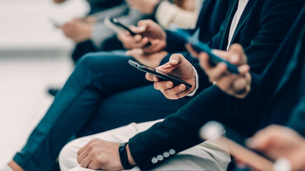 Gruppe verschiedener junger Leute mit Smartphones, die in einer Reihe sitzen