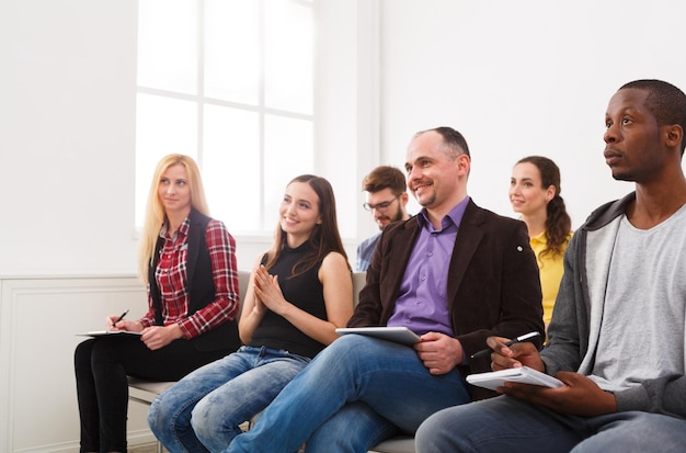 Gruppe verschiedener multiethnischer, fröhlicher Zuhörer, die auf Konferenz sitzen, Raum kopieren