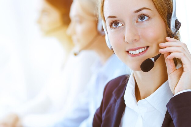 Foto gruppe verschiedener telefonisten bei der arbeit im sonnigen büro. hübsche geschäftsfrau mit kopfhörern, die kunden beraten. konzept für call center und geschäftsleute.