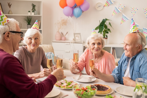 Gruppe von älteren Leuten, die durch gedienten Tisch zu Hause sitzen, während Geburtstag feiern