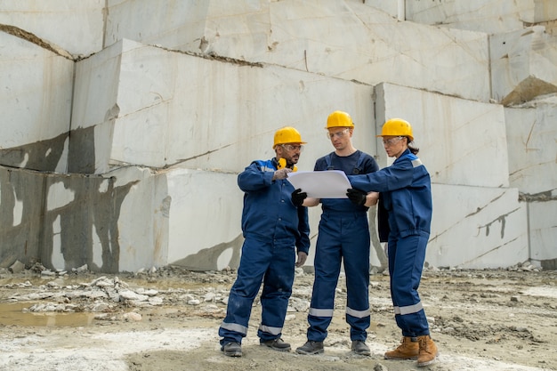 Gruppe von Bauherren, die während der Arbeit eine Skizze auf einer entfalteten Blaupause besprechen