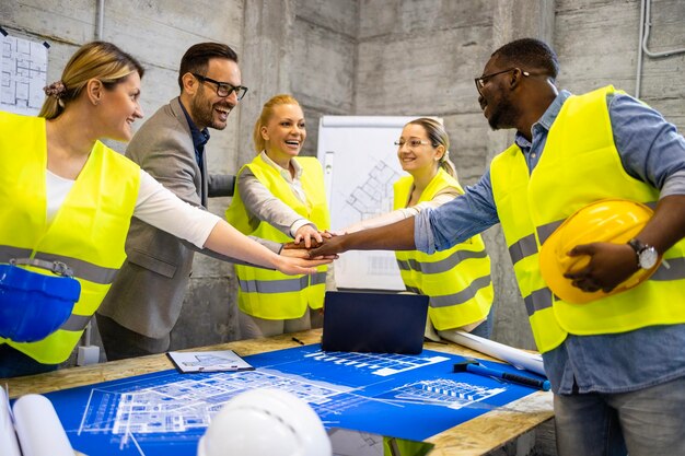 Gruppe von Bauingenieuren und Architekten, die sich über Bauplänen an den Händen halten