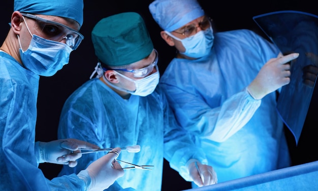 Gruppe von Chirurgen bei der Arbeit im Operationssaal, blau getönt Medizinisches Team, das die Operation durchführt