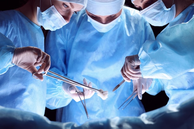 Gruppe von Chirurgen bei der Arbeit im Operationssaal blau getönt. Medizinisches Team, das Operation durchführt