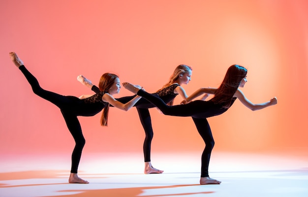 Gruppe von drei Ballettmädchen in schwarzen eng anliegenden Anzügen, die auf einem roten Hintergrund tanzen