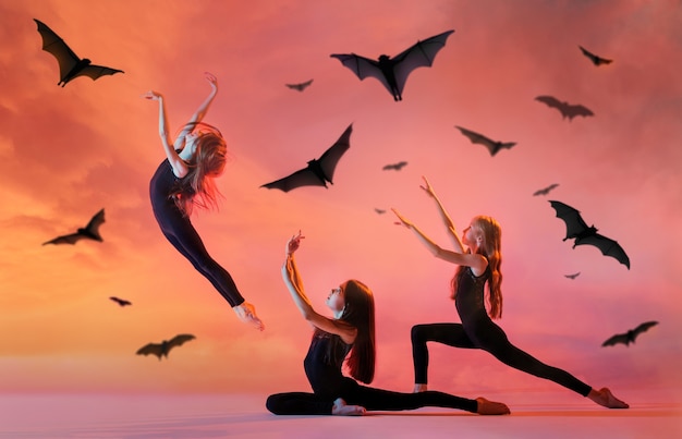 Gruppe von drei kleinen Ballerinas mit langen wallenden Haaren in schwarzen eng anliegenden Kostümen, die auf rotem Hintergrund mit Fledermäusen tanzen