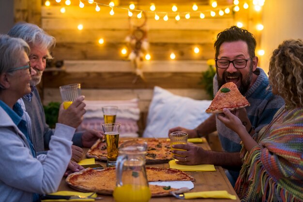 Gruppe von Erwachsenen zusammen auf dem Holztisch, die in der Weihnachtsnacht zwei große Pizzen isst - Familie im Freien beim Abendessen