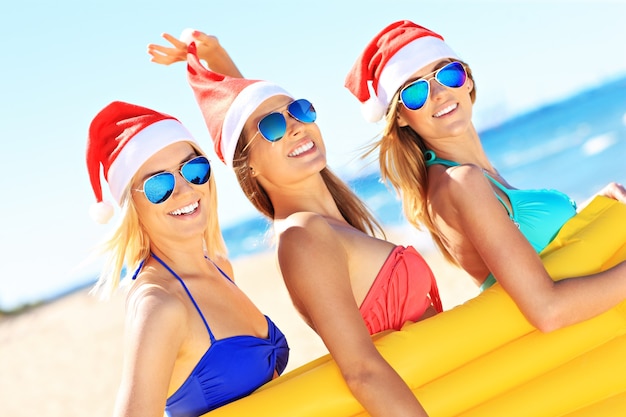 Gruppe von Frauen im Bikini und Weihnachtsmützen mit Matratze am Strand