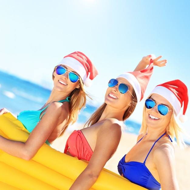 Gruppe von Frauen im Bikini und Weihnachtsmützen mit Matratze am Strand