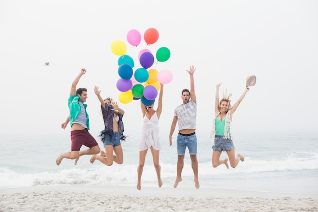 Gruppe von Freunden am Strand mit Luftballons springen