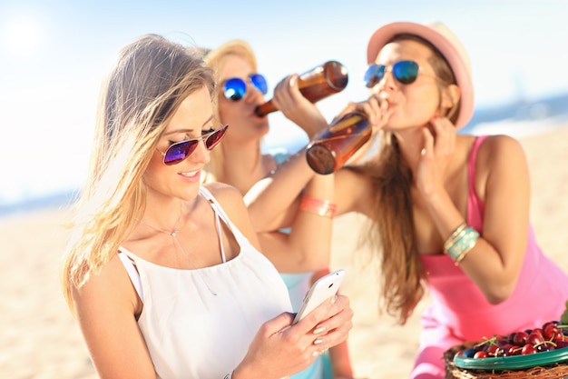 Gruppe von Freunden, die am Strand Bier trinken und SMS schreiben?