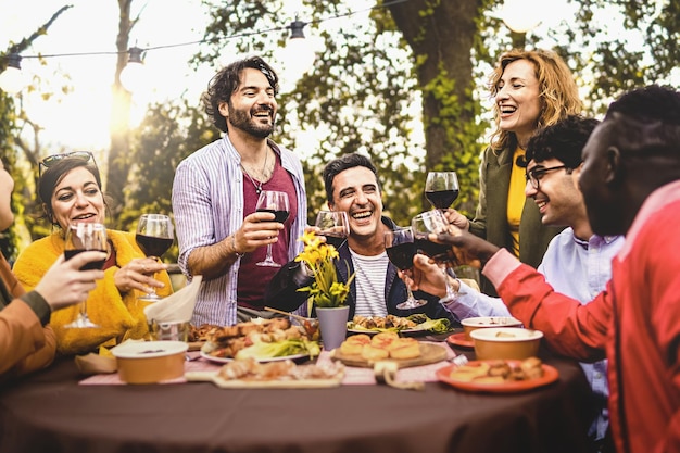 Gruppe von Freunden, die im Freien speisen und mit Rotwein im Hinterhof anstoßen. Menschen mit mehreren Generationen, die gemeinsam Spaß in der Natur haben und am Esstisch sitzen, konzentrieren sich auf den reifen Mann