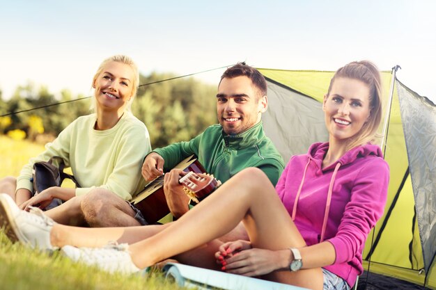 Gruppe von Freunden, die im Wald campen und Gitarre spielen playing