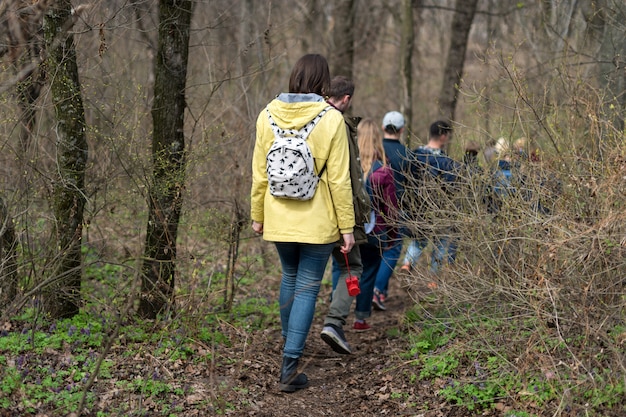 Gruppe von Freunden, die mit Rucksäcken im Frühlingswald von hinten gehen. Backpacker, die im Wald wandern. Abenteuer, Reisen, Tourismus, aktive Erholung, Wanderung und Menschenfreundschaftskonzept.