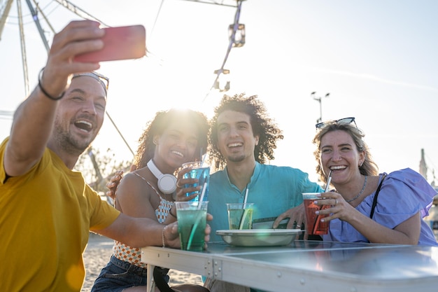 Gruppe von Freunden, die sich auf einer Picknickparty selbst machen vier junge Leute, die sich am Strand amüsieren und Inhalte in sozialen Netzwerken mithilfe von Technologie und Smartphone-App teilen