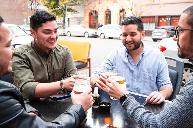 Gruppe von Freunden, die vor einer Bar sitzen, miteinander reden und mit Craft Beer anstoßen