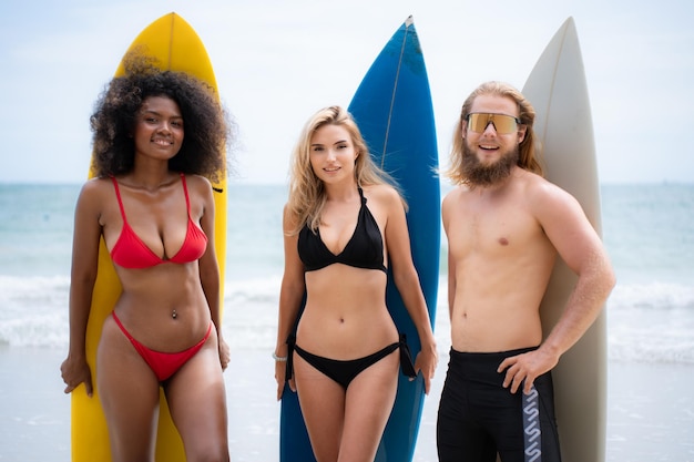 Foto gruppe von freunden in badeanzügen, die mit surfbrettern am strand posieren