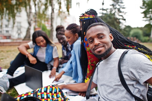 Gruppe von fünf afrikanischen College-Studenten, die Zeit miteinander auf dem Campus des Universitätshofs verbringen Schwarze Afro-Freunde sitzen auf Gras und lernen mit Laptops