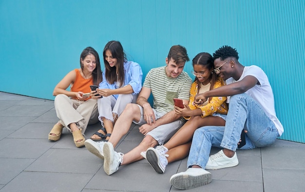 Gruppe von fünf multiethnischen Studentenfreunden sitzen auf dem Boden in der Schule und benutzen Smartphones