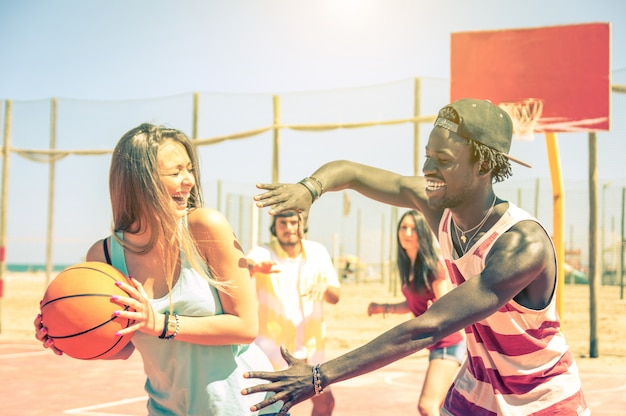 Gruppe von gemischtrassigen glücklichen teenagern, die im freien basketball spielen - kaukasier und schwarze - konzept über sommerferien, sport, spiele und freundschaft