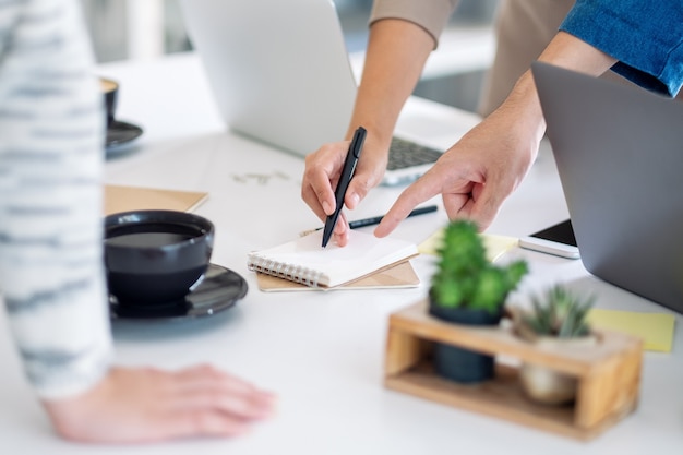 Foto gruppe von geschäftsleuten, die im büro diskutieren, schreiben und mit dem finger auf das notebook auf dem tisch zeigen