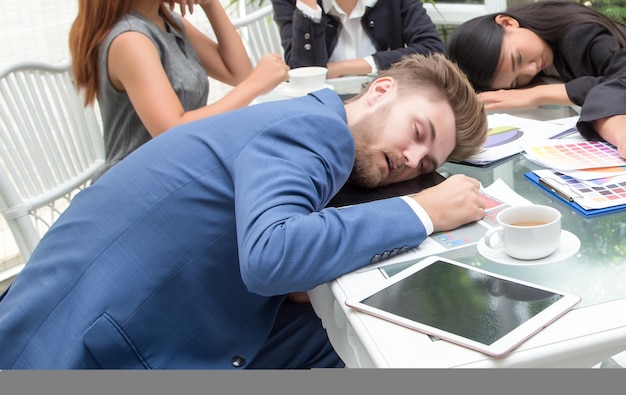 Gruppe von Geschäftsleuten, die während des Arbeitstreffens im Konferenzraum schlafen, Männer und Frauen sitzen entspannt am Schreibtisch mit geschlossenen Augen