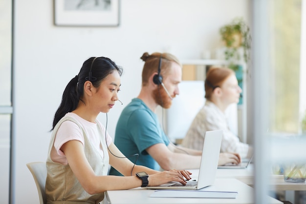 Gruppe von Geschäftsleuten in den Kopfhörern, die am Tisch sitzen und an Laptop-Computern im Büro arbeiten