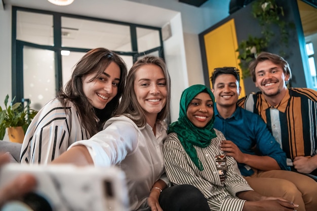 Gruppe von Geschäftsleuten während einer Pause von der Arbeit, die ein Selfie-Foto macht, während sie die Freizeit im Entspannungsbereich eines modernen Großraum-Startup-Büros genießen. Selektiver Fokus. Hochwertiges Foto