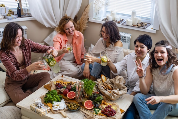 Gruppe von glücklichen Freundinnen, die zusammen bei henparty mit gesundem Essen und Trinken posieren