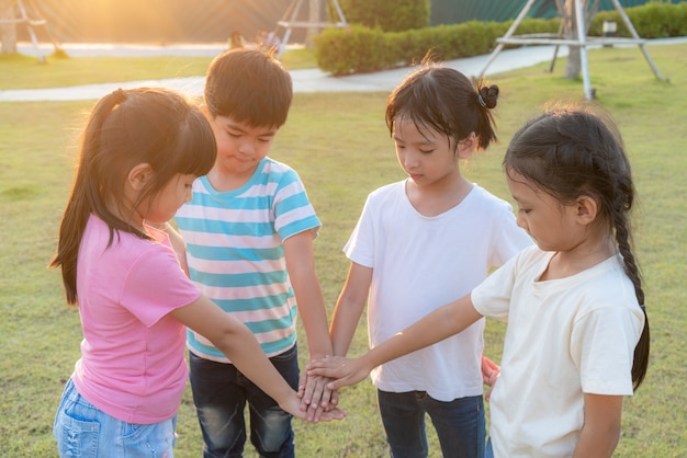 Gruppe von glücklichen jungen asiatischen Kindern stapeln oder stapeln Hände zusammen draußen im Stadtparkspielplatz am Sommertag. Kinder- und Erholungskonzept.