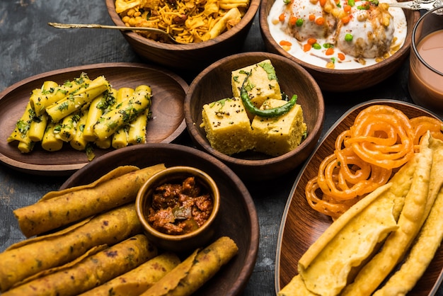 Foto gruppe von gujarati-snacks wie jalebi-fafda, thepla, khaman dhokla, aloo bhujiya, khandvi, khakra, dahi vada, gathiya mit heißem tee