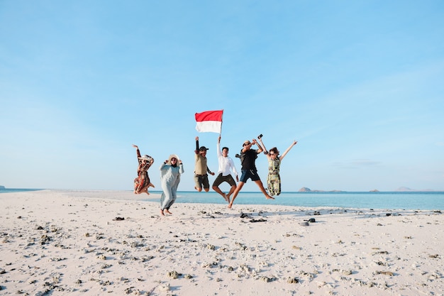 Gruppe von Indonesiern, die mit einem Mann, der die indonesische Flagge hält, am Strand springen