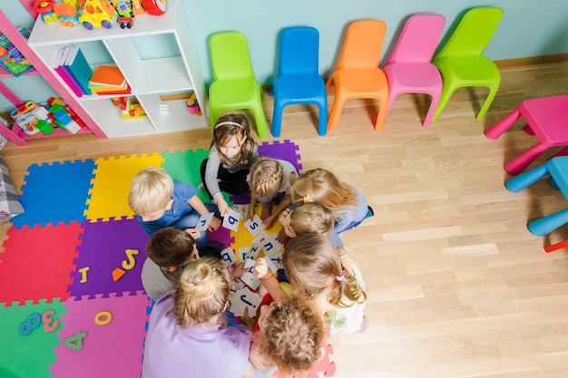 Gruppe von Kindergartenkindern, die zusammen mit Lehrern, die Gruppenarbeit leisten, eng auf einem Boden sitzen Kinder lernen, beim Lösen von Aufgaben zusammenzuarbeiten