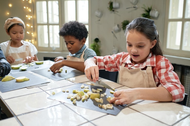 Gruppe von Kindern, die zusammen am Tisch frische Früchte auf einem Schneidebrett schneiden