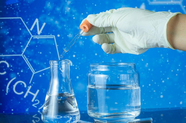 Gruppe von Laborflaschen leer oder gefüllt mit einer klaren Flüssigkeit auf blau getönten wissenschaftlichen Grafiken zurück