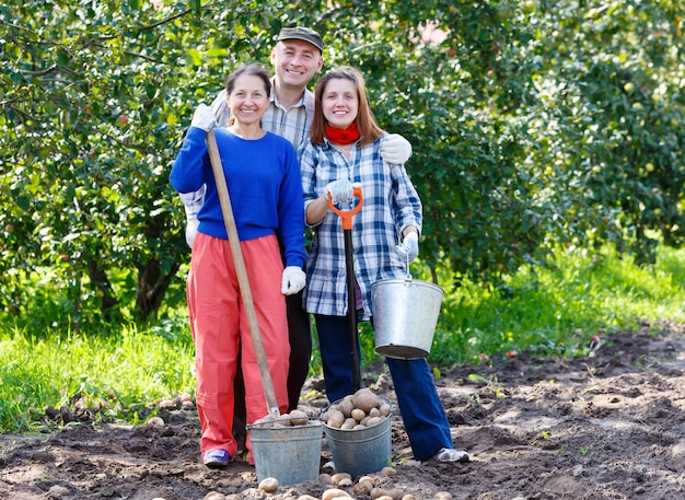 Gruppe von Leuten im Garten mit einer Eimerschaufel, die Kartoffeln pflanzt