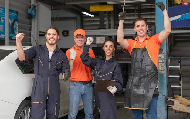 Gruppe von Mechanikern und -frauen, die die Hände heben, um in der Autowerkstatt erfolgreich zu arbeiten