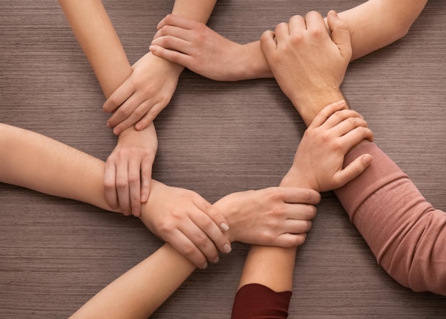 Gruppe von Menschen, die mit ihren Händen einen Kreis auf einem hölzernen Hintergrund bilden. Einheitskonzept