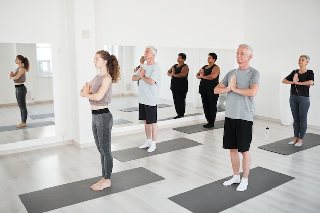 Gruppe von Menschen mit Lehrer, die zusammen mit geschlossenen Augen während des Yoga-Kurses im Studio meditieren