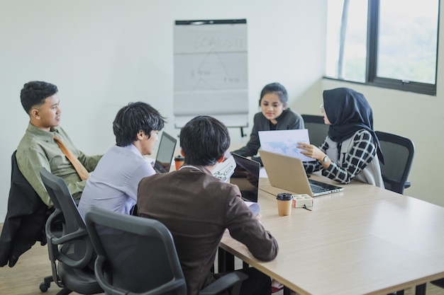 Gruppe von Mitarbeitern, die ein Geschäftstreffen im Büro haben. Muslimische Frau legt anderen Papierkram vor.