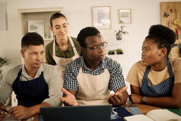 Gruppe von Modestudenten oder Designern, die Brainstorming betreiben und über Kleidung sprechen, die sich Notizen in Buch und Laptop macht Verschiedene Schneider lernen etwas über Denim-Stoffe und Materialien und diskutieren Stile oder Trends