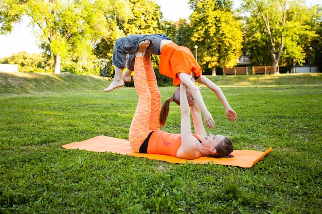 Gruppe von Müttern und ihren Kindern, die Yoga auf Fitnessteppichen an der frischen Luft praktizieren?