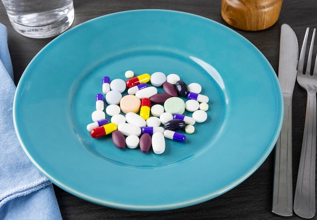 Gruppe von Pillen, Kapseln und anderen Medikamenten über einem Teller auf einem Esstisch