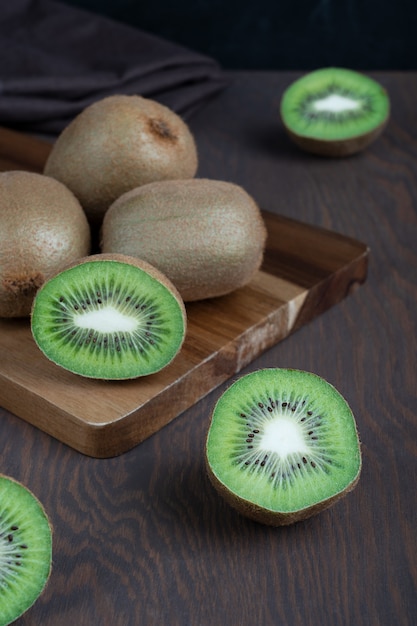 Gruppe von reifen saftigen Kiwis auf Schneidebrett auf dunkelbraunem Holztisch