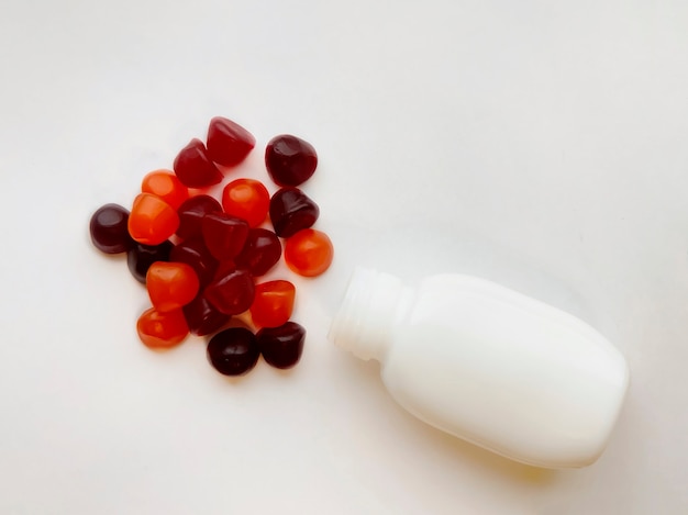 Gruppe von roten, orangefarbenen und violetten Multivitamin-Gummis mit der Flasche isoliert auf weißem Hintergrund. Gesundes Lebensstilkonzept.