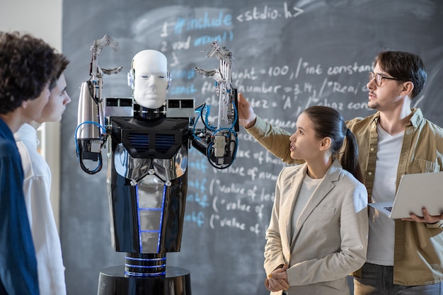 Foto gruppe von schülern, die computersteuerungsroboter mit erhobenen händen betrachten, während ihr lehrer seine fähigkeiten im unterricht demonstriert
