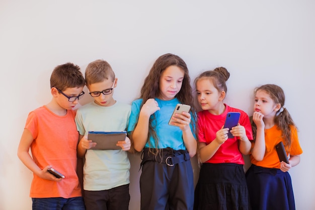 Gruppe von Schuljungen und Schulmädchen in bunten T-Shirts, die die Pause verbringen, nicht draußen rennen oder spielen, sondern auf ihre Gadgets schauen Kinder, die sich für Online-Chat statt für Interaktion im Leben entscheiden